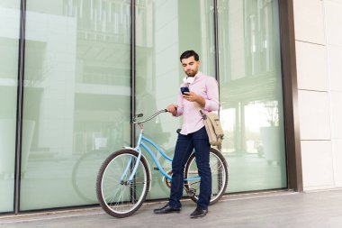 İşe vardıktan sonra bisikletinin yanındaki akıllı telefondan çevre dostu ulaşımla mesaj atan meşgul bir iş adamı. 