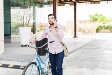Şehirdeki işe bisikletle gidip gelirken akıllı telefondan iş görüşmesi yapan genç Latin bir adam.