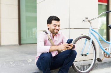 Heyecanlı genç adam işe bisikletle gittikten sonra telefonuyla mesajlaşırken şehirde dinleniyor.