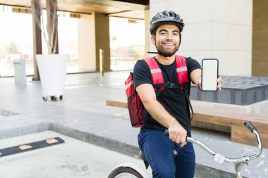 Teslimatçı olarak çalışan heyecanlı genç adam yemek dağıtım uygulamasını kullanırken ve bisiklet sürerken akıllı telefon ekranını gösteriyor.