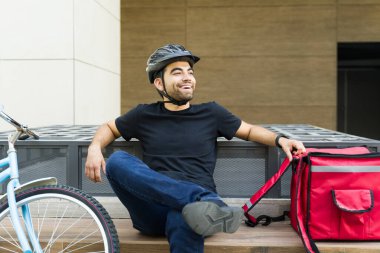 Genç adam gülerken ve mutlu görünürken teslimatçı olarak çalışırken yemek dağıtırken ve bisiklet sürerken.