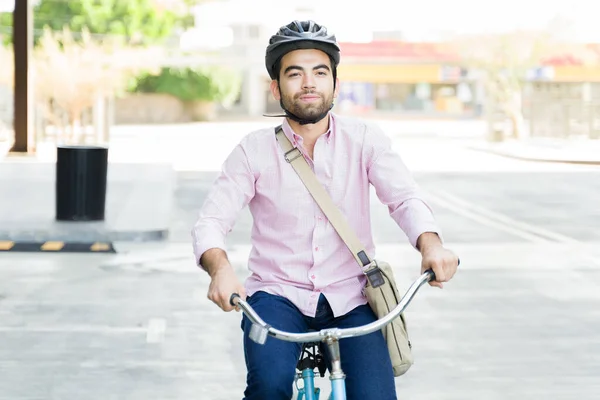 Casual business man smiling wearing a helmet while riding his bicycle commuting to work looking happy