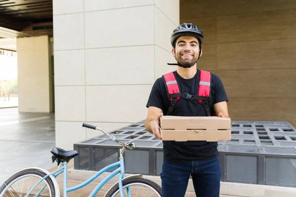 ピザを持っている陽気な配達人と笑顔自転車に乗って街で食べ物を配達しながら — ストック写真