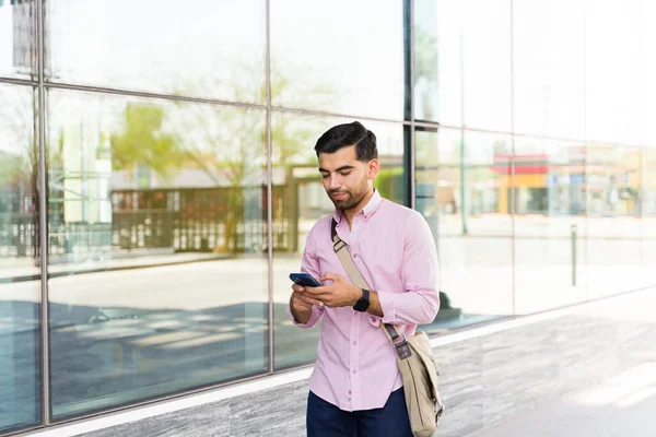 スマートフォンにテキストメッセージを送りながら通勤中に街を歩く魅力的なラテン人 — ストック写真