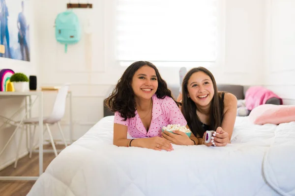 リラックスした十代の女の子はベッドに横たわって笑いながら映画を見ながらパジャマと食べるポップコーン — ストック写真