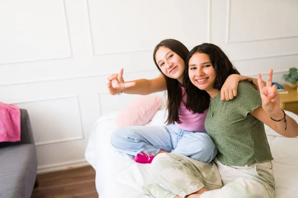 幸せな十代の女の子作る平和のサインと笑顔を楽しみながら一緒にベッドルームでアイコンタクト — ストック写真