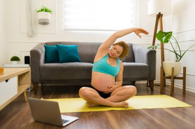 Hamile kadın evden online kurs alırken esneme egzersizleri yapıyor ve ısınıyor.