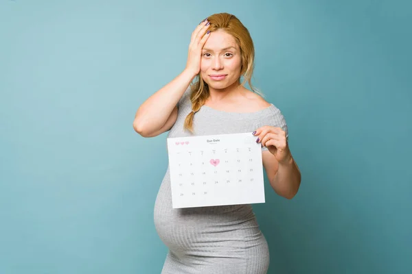 Kobieta Trzydziestce Wyglądająca Zestresowaną Zaniepokojoną Terminem Porodu Trzymająca Kalendarz Studiu — Zdjęcie stockowe