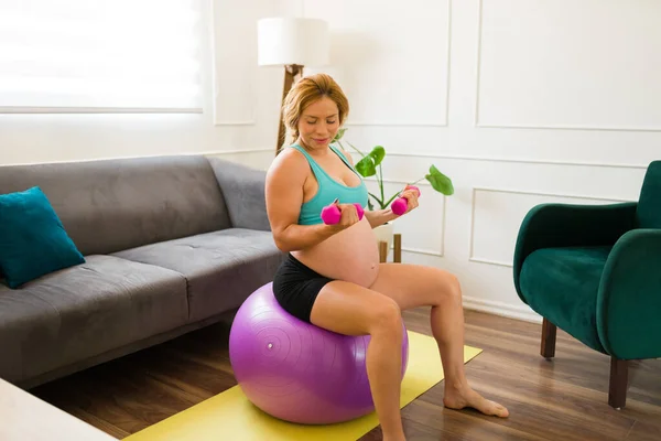 穿着运动服的准妈妈坐在家里的稳定球上举重 — 图库照片