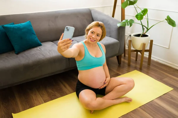一个穿着运动服的漂亮孕妇准备锻炼并拿着智能手机自拍的画像 — 图库照片
