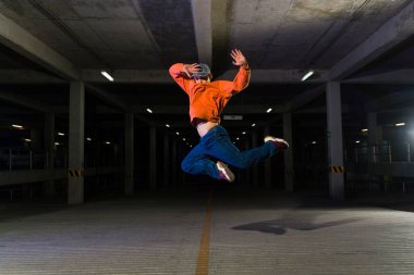 Aktif sokak dansçısı geceleri karanlık bir otoparkta modern havalı müzikle havaya atlayıp dans ediyor.