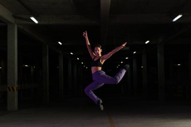 Heyecanlı Latin bayan modern dansçı havaya atlarken neşeli görünüyor ve modern havalı bir dans yapıyor. 