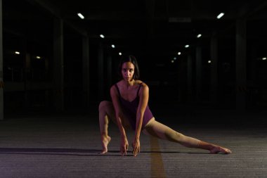 Artistik modern dansçı gece dans ederken esnek görünüyor. Park yerinde kameraya bakarak sanatsal bir performans sergiliyor.