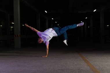 Havalı genç adam ve sokak sanatçısı break dans yapıyor ya da karanlık bir otoparkta modern dans yapıyor.
