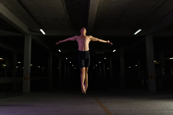 현대의 예술적 무용수가 어두운 주차장에서 발레를 하면서 공중으로 뛰어오르는 — 스톡 사진