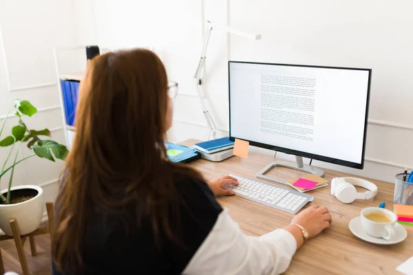 スクリーンを見ながら彼女のオフィスで働くと彼女の机のコンピュータを使用して後ろから見たプロの大女性 — ストック写真