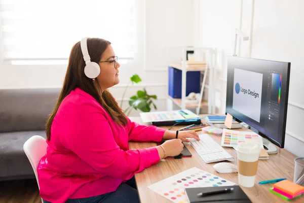 美しいラテン語の女性とグラフィックデザイナーヘッドフォンで音楽を聴き 仕事でコンピュータ上で設計 — ストック写真