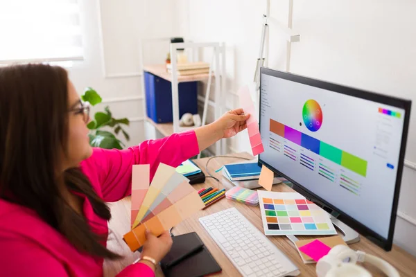 女设计师一边在电脑上工作 一边看着彩色石碑 并为标识选择新的色彩设计 — 图库照片