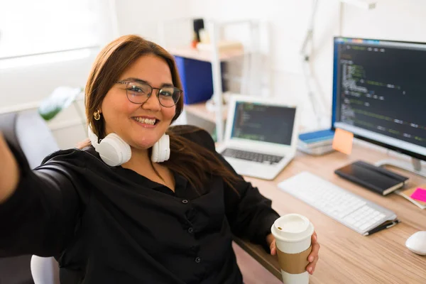 彼女のオフィスの机で仕事とコーディングをしながら幸せそうな顔をしているヒスパニック脂肪のプログラマーの個人的な視点と自撮り — ストック写真
