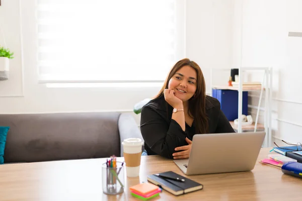 管理責任者として働く魅力的なプラスサイズの女性とコーヒーと彼女のオフィスの机に座っている間 カメラに笑顔 — ストック写真