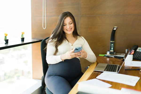 Sorrindo Grávida Empresária Sentada Sua Mesa Mensagens Texto Seu Celular — Fotografia de Stock