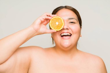30 'lu yaşlardaki şişman bir kadın kırışıklıkları ve yaşlanmayı önlemek için C vitamini kullanırken çıplak omuzlarıyla eğleniyor.