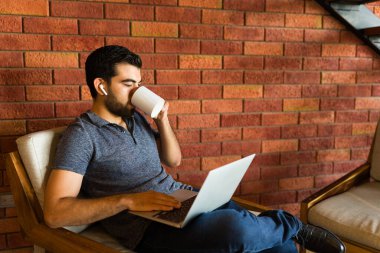 Kulaklıklı çekici latin adam laptopta yazarken kahve içiyor ve uzaktan kumandayla serbest çalışıyor.