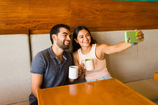 在咖啡店边喝咖啡边用手机自拍 一边笑着吸引人的两位朋友 — 图库照片