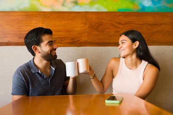 リラックスしたカフェでのデート中に一緒にコーヒーを飲みながら笑顔を浮かべている間に魅力的な幸せなカップルの乾杯 — ストック写真