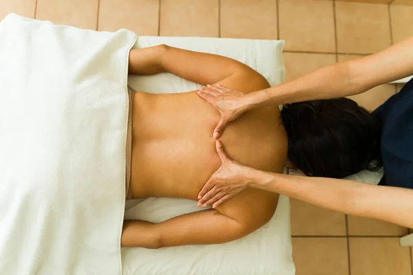 Latin relaxed young woman at the massage table at the wellness spa center getting a relaxing treatment from a therapist