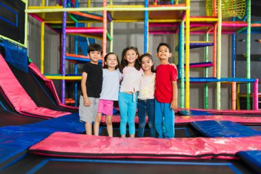 Mutlu çocuklar sarılıyor ve oyun parkının trambolin alanında birlikte oyun oynuyorlar.