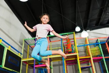 Eğlenceli oyun odasındaki trambolin bölgesinde çocuklarla oynarken havaya atlayan beyaz güzel bir kız.