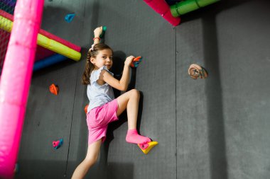 Oyun oynarken gülümseyen ve çocuklarla kaya tırmanışı yapan mutlu bir çocuk. Arkadaşları oyun odasında neşeli görünüyorlar.