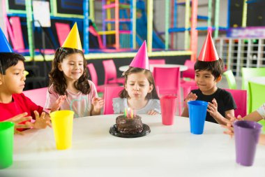 Parkta oynadıktan sonra pasta mumlarını üflerken güzel bir çocuk arkadaşlarıyla doğum günü partisini kutluyor.