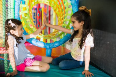 Latin kız en iyi arkadaşıyla oynarken gülüyor ve kapalı alandaki oyun bahçesinde oyun öncesi beşlik çakıyor.