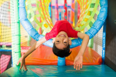 Heyecanlı genç çocuk renkli oyun bahçesinde eğleniyor baş aşağı oynuyor ve eğlenceli oyunu sırasında gülüyor. 