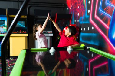 Heyecanlı çocuklar oyun odasında arkadaşlarıyla hava hokeyi müsabakası kazanarak beşlik çakıyorlar.