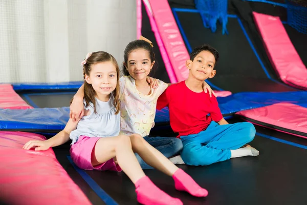 Sevimli çocuklar trambolin bölgesinde oynarken kameraya bakıp gülümsüyor.
