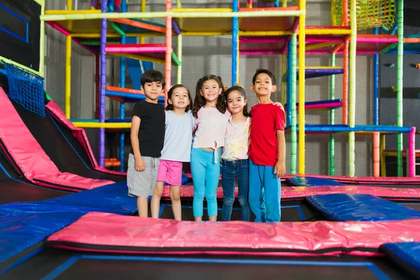 Mutlu çocuklar sarılıyor ve oyun parkının trambolin alanında birlikte oyun oynuyorlar.