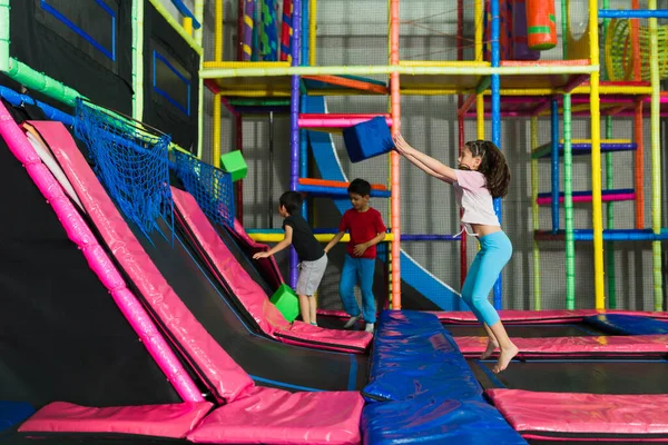 Neşeli bir grup çocuk topla oynuyor ve trambolin bölgesinde birlikte eğleniyorlar.