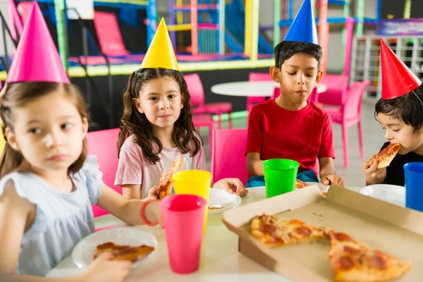 Adorable children wearing party hats and celebrating a fun birthday party eating pizza with friends in the playground