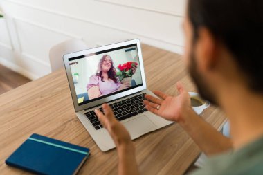 Bilgisayarda çiçek alan bir video görüşmesi sırasında kız arkadaşıyla konuşan genç bir adamın arka görüntüsü.