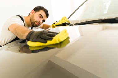 İspanyol erkek işçi, oto temizlik servisinde mikrofiber bez kullanarak temizlik arabasının kaputunu kullanıyor.