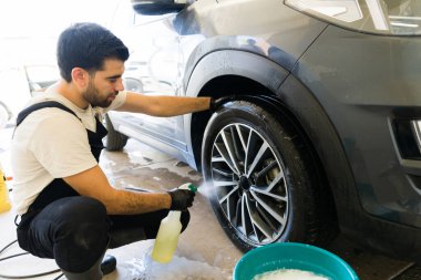 Araba yıkamada tekerlekleri yıkamak için sabun spreyi kullanan iyi görünümlü bir işçi.