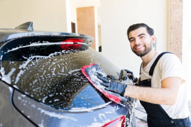 Yakışıklı, genç, İspanyol bir erkek, araba yıkama servisinde araba yıkıyor.