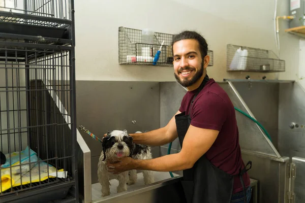 Köpek tımarcısı olarak çalışırken gülümseyen ve tıraş olmadan önce ıslak bir köpeğe banyo yaptıran mutlu İspanyol adam.