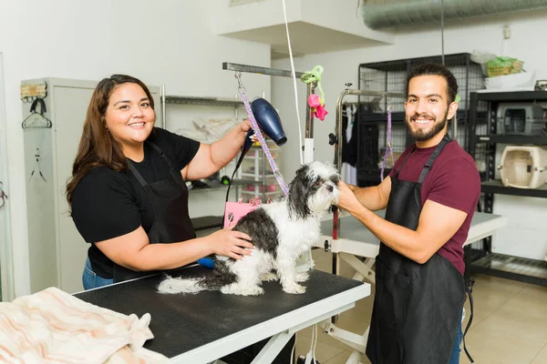 Happy latin pet groomers looking at the camera while working in the grooming services of a shih tzu after a bath