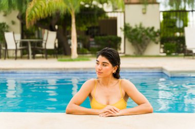 Yirmili yaşlardaki Meksikalı genç bir kadın yazın açık havada yüzdükten sonra havuzda seksi görünüyor. 