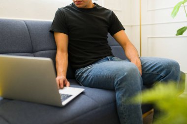 Evde siyah bir tişört giyerken internette alışveriş yapan genç bir adam.