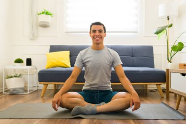 Çekici bir genç adam evde yoga yapıyor spor yaparken spor yaparken jimnastik gri tişörtü giyiyor. 